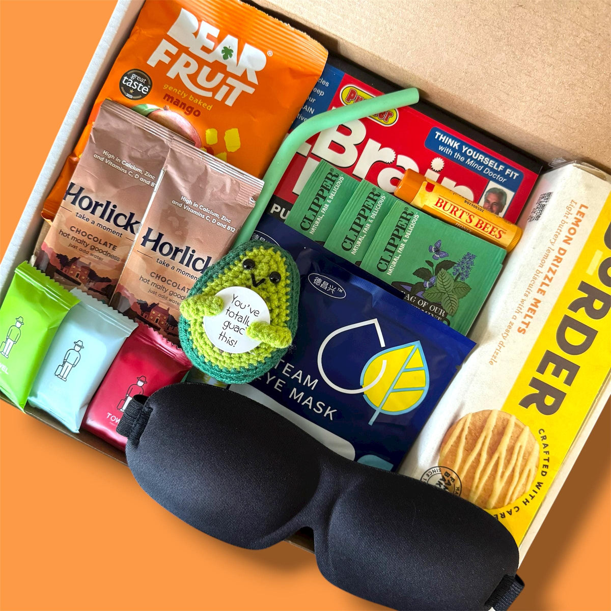 Assorted items including a sleep mask, snacks, and health products in a box on an orange background