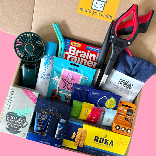 Hysterectomy recovery care package with cooling mist spray, sleep products, snacks, heat pack, grabber tool and thoughtful comfort items arranged in an open gift box.