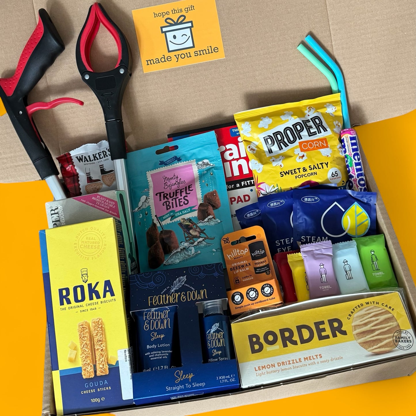 Assorted snacks and items in a box with visible branding on a cardboard background.