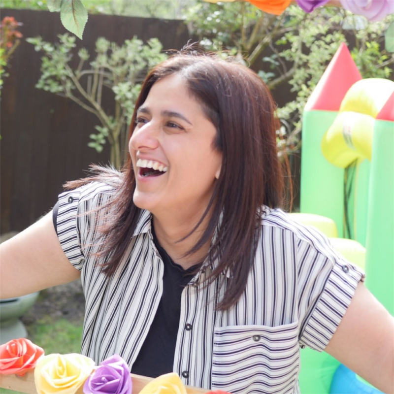 Woman laughing outdoors with colorful balloons and a tree in the background