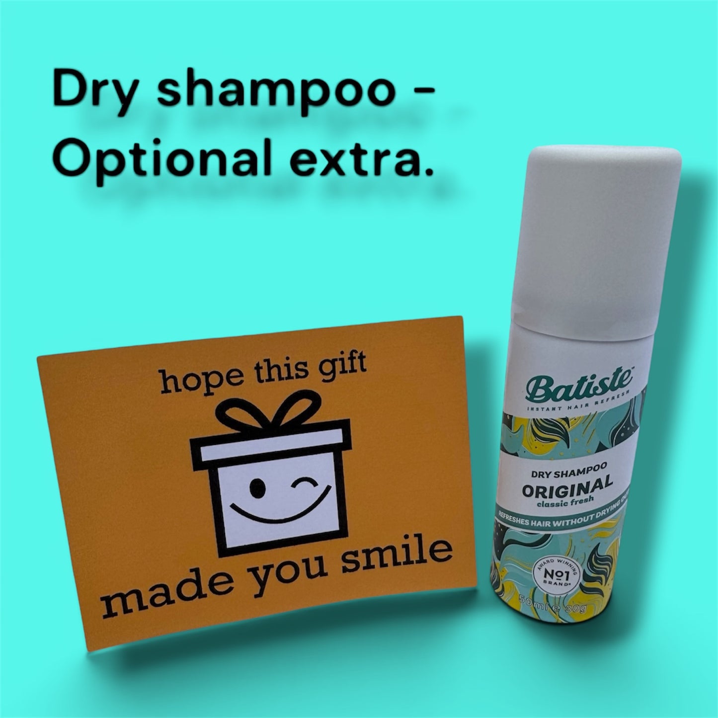 A bottle of Batiste Dry Shampoo Original next to a brown gift card with a smiley face gift box graphic and the text 'hope this gift made you smile', set against a bright turquoise background with text reading 'Dry shampoo - Optional extra.'.