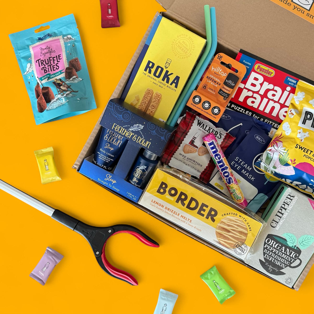 Open box containing various snacks and products on a yellow background with scissors.